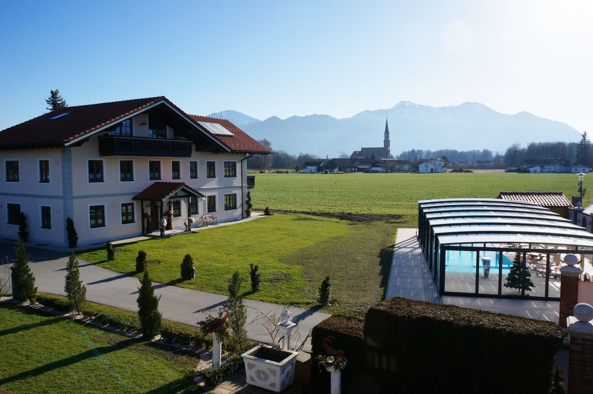 Farm with garden and flowers, green meadows with grazing cows and mountains under clear skies in the background