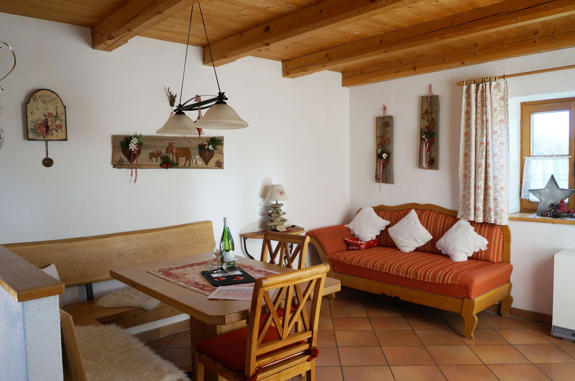 Cozy sitting area with wooden table, corner bench, red sofa with white cushions, and decorations on white walls